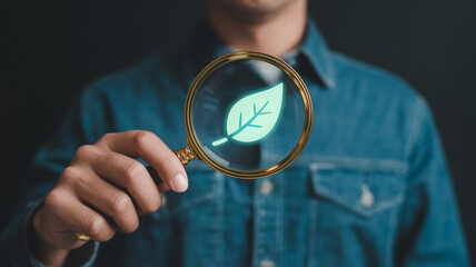Examining sustainability practices a man holding a magnifying glass over a green leaf icon concept