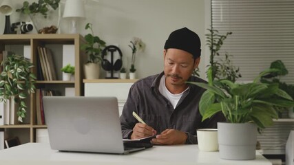 Asian man writing notes at home office desk.4k - Powered by Adobe