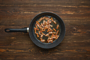 Cooking crispy bacon in a frying pan on a rustic wooden table