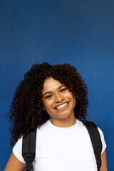 Fototapeta premium Young student smiling with backpack on blue background
