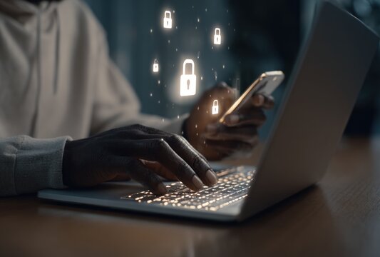 A person types on a laptop while holding a phone, with illuminated padlock icons floating above the screen, symbolizing security