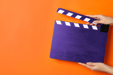 Woman holding purple clapperboard on orange background, closeup with space for text. Film industry