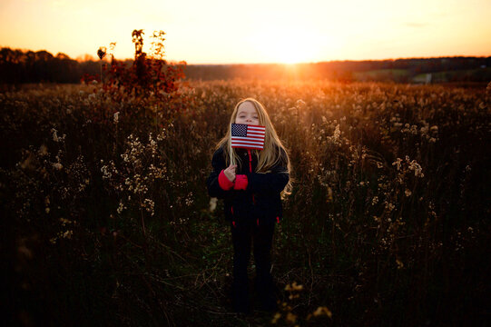 Beautiful happy young girl holding American flag in sunny field - Powered by Adobe