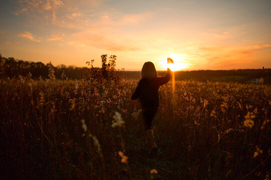 Behing young girl walking through sunset field holding American