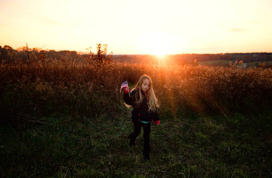 Beautiful young girl walking through sunny field waving American