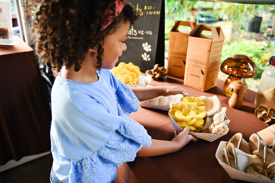Child holding tray of fresh oyster mushrooms at market stand - Powered by Adobe