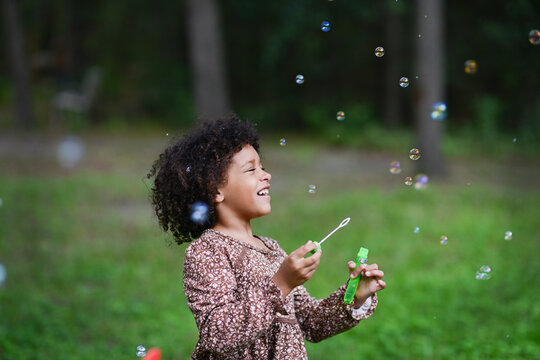 Laughing girl blows bubbles in grassy outdoor area.