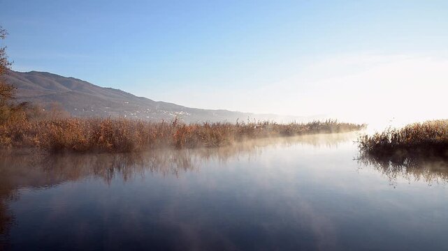 Fog and mist on the lake with flat waters  in the early morning. Lake Varese, Bardello area and in the background the regional park of Mount Campo dei Fiori of Varese, Italy