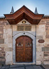 Dervishan Door, an ornate wooden entrance to Mevlana Museum, set in a stone facade with calligraphic details. Konya, Turkey