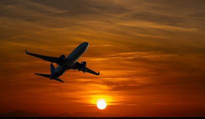 Obraz premium Silhouette of a passenger airplane taking off against a dramatic orange sunset sky with clouds and mountains on the horizon. Perfect for travel, aviation, holiday, and adventure concepts.