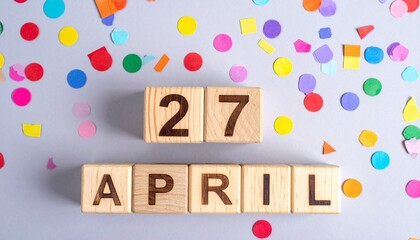 Wooden Blocks with Date 27 April. Calendar for birthday or anniversary on solid colored background with confetti