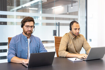 Customer service representatives working in modern office using laptops and headsets