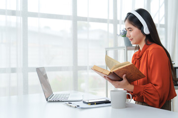 Young woman reading a book while following online lesson on laptop