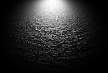 Dramatic lighting highlights a dark, uneven surface with textures resembling rock or sand, creating a moody and abstract background
