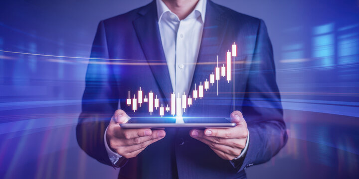 A businessman in a suit holds a tablet displaying a rising stock market graph with a futuristic blue background.