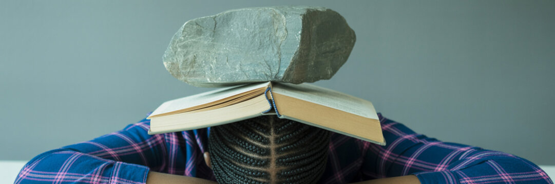 Overwhelmed student with rock on head studying hard for exam preparation stress and academic pressure