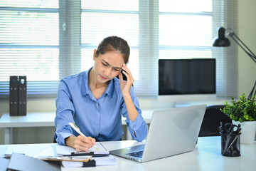 Stressed businesswoman working at desk with laptop and documents in an office