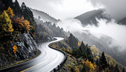A scenic view of a winding road climbing a misty mountain range. Autumn trees with yellow leaves line the wet asphalt, creating a dramatic, cloudy landscape.