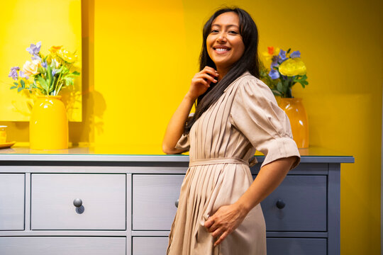 Smiling woman standing by cabinet with flowers in modern yellow interior