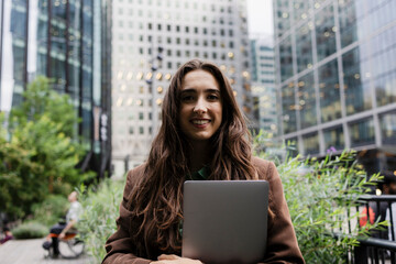Businesswoman with laptop smiling outdoors in London financial district