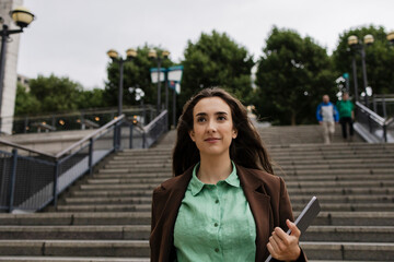 Businesswoman walking outdoors on city stairs holding tablet