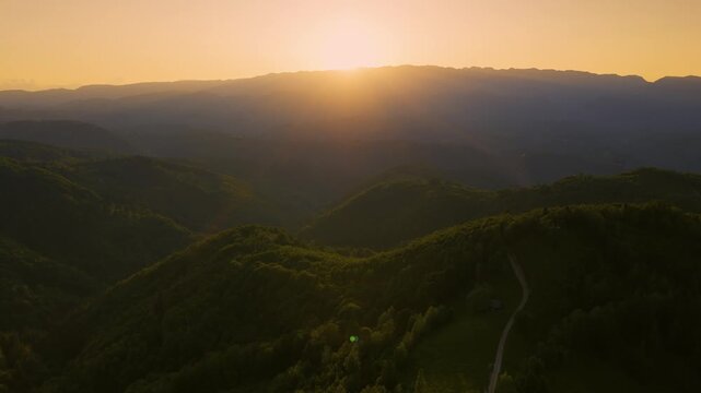 Aerial sunset view over Bran Rucar corridor with rolling green hills, traditional villages Moeciu Fundata Sirnea Pestera Magura, forests and Piatra Craiului silhouette, Transylvania Romania