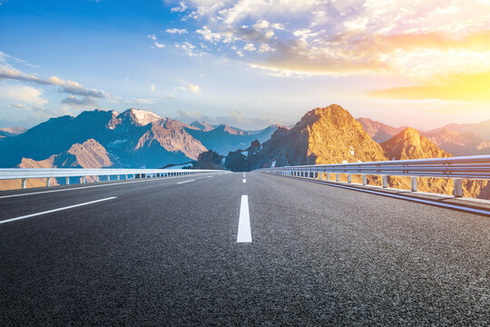 Empty asphalt highway road leads to majestic mountain natural landscape at a beautiful golden sunrise - Powered by Adobe