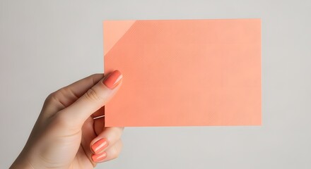 Obraz premium Hand holding an orange card for presentation or message with painted nails on a light background