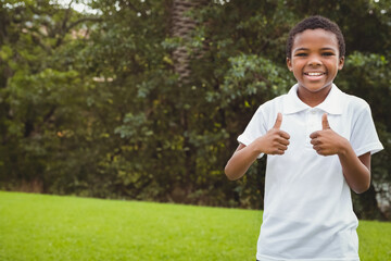Smiling African American boy wearing white shirt in park giving thumbs up to camera, copy space