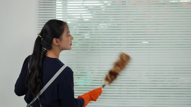 Housekeeper cleaning venetian blinds with feather duster
