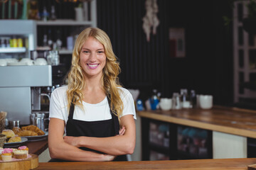 Female barista standing at cafe wearing apron arranging pastries and operating espresso machine