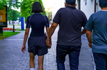 Obraz premium Group of three people walking hand in hand in an urban park on a sunny day