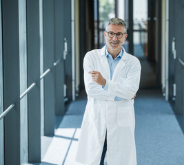 Confident doctor in lab coat smiling in modern office corridor