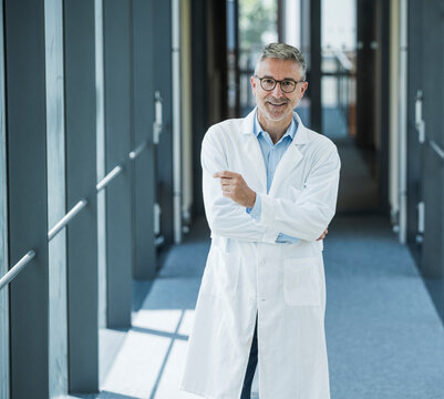 Confident doctor in lab coat smiling in modern office corridor