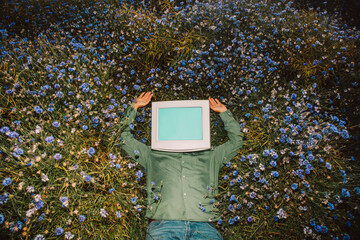 Person with CRT monitor head lying in summer wildflower meadow relaxing