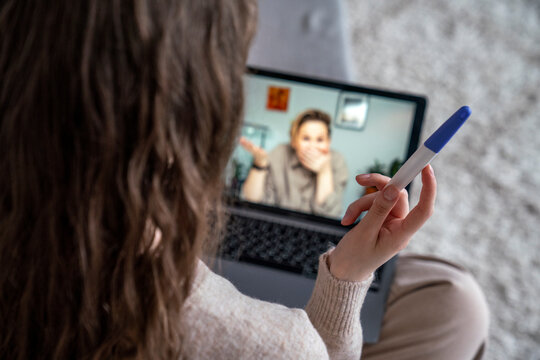 Woman with pregnancy testing kit talking to friend on video call over laptop