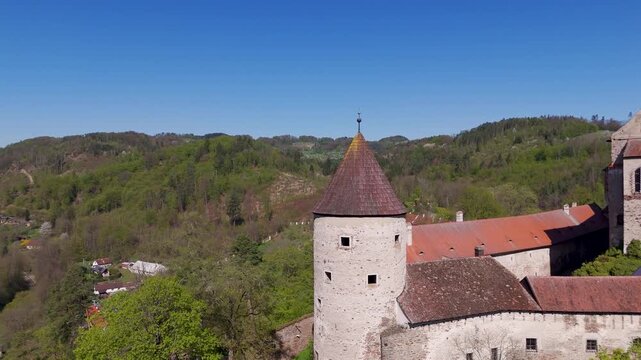 Aerial drone pans slowly around the massive circular tower of Pernstein Castle, showcasing the Gothic stone walls perched above the lush Nedvedice landscape in South Moravia, Czechia.