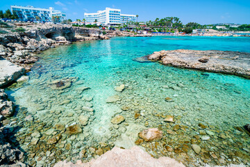 Tourists relax on Cypriot beach in bay with turquoise waters at seaside resort Nisia Loumbardi,...