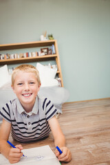 Child drawing in notebook with pen on bedroom floor near bookshelf with plant, copy space