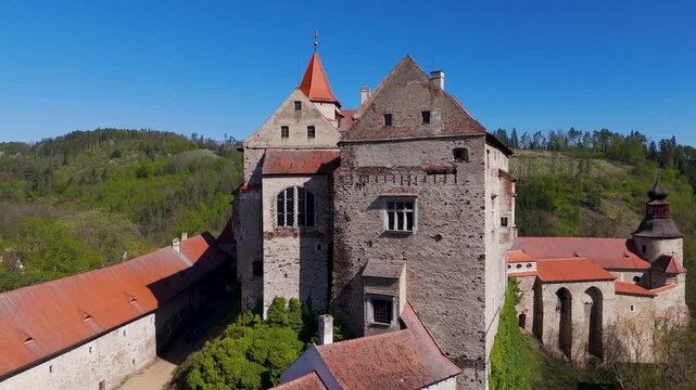 Aerial drone pull-out shot dramatically revealing the majestic Gothic and Renaissance Pernstein Castle perched high on a massive rock formation above Nedvedice, South Moravia, Czechia.