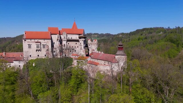Aerial drone shot flying directly toward the majestic Pernstein Castle, showcasing the historic Gothic and Renaissance fortress perched on its rock above Nedvedice, Czechia.