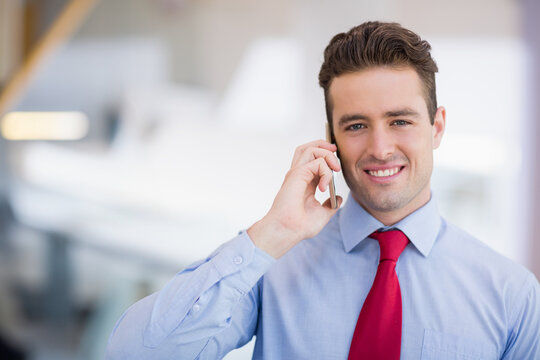 Businessman talking on smartphone while smiling in modern open-plan office, copy space - Powered by Adobe