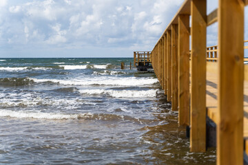 A picturesque wooden pier gracefully extending into the vast ocean beneath a vibrant sky and gentle waves, Bastad, Sweden