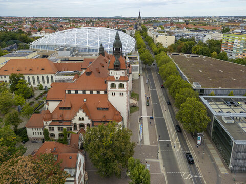 Aerial view of the vibrant, red-roofed Leipziger Zoo buildings contrasting against the modern, white-framed structure, bisected by a tree-lined street, Leipzig, Saxony, Germany.