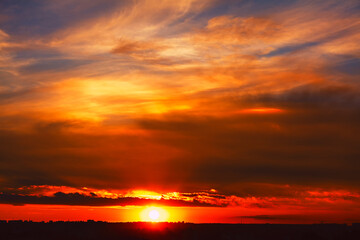 Dramatic sunset across the sky. Sun below the horizon, casting a fiery glow on the clouds. Twilight view with a rich palette of warm colors