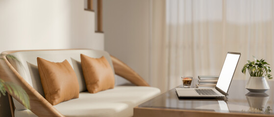 Laptop and coffee on glass top wooden table and sofa beside stairs in a living room of modern house