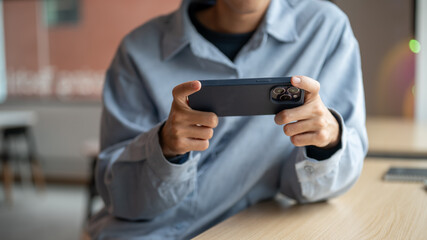 Close up of man looking at phone holding horizontal playing game or watching video at table in cafe.