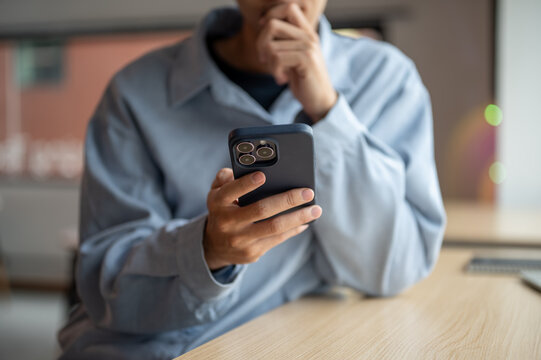 Close up of a man looking at smartphone with hand holding chin while sitting at wooden table in cafe