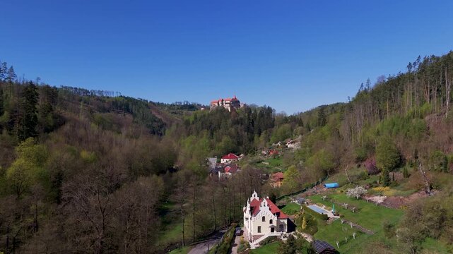 Aerial drone shot approaching the iconic Pernstein Castle in Nedvedice, South Moravia, Czech Republic, highlighting the medieval Gothic and Renaissance architecture against a clear spring sky.