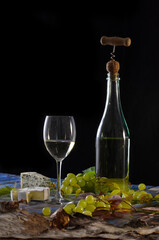 Obraz premium Bottle of white wine with corkscrew, glass of white wine, green grapes and blue cheese on black background.